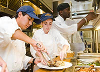 FIU-Lunch-4347 - FIU School of Hospitality and Tourism students Line cooks Jose Pardave, left, Denise Martinez, center, and teaching assistant Jouvens Jean prepare the dishes of the main course during a luncheon at the college's Biscayne Campus in Miami.<br>